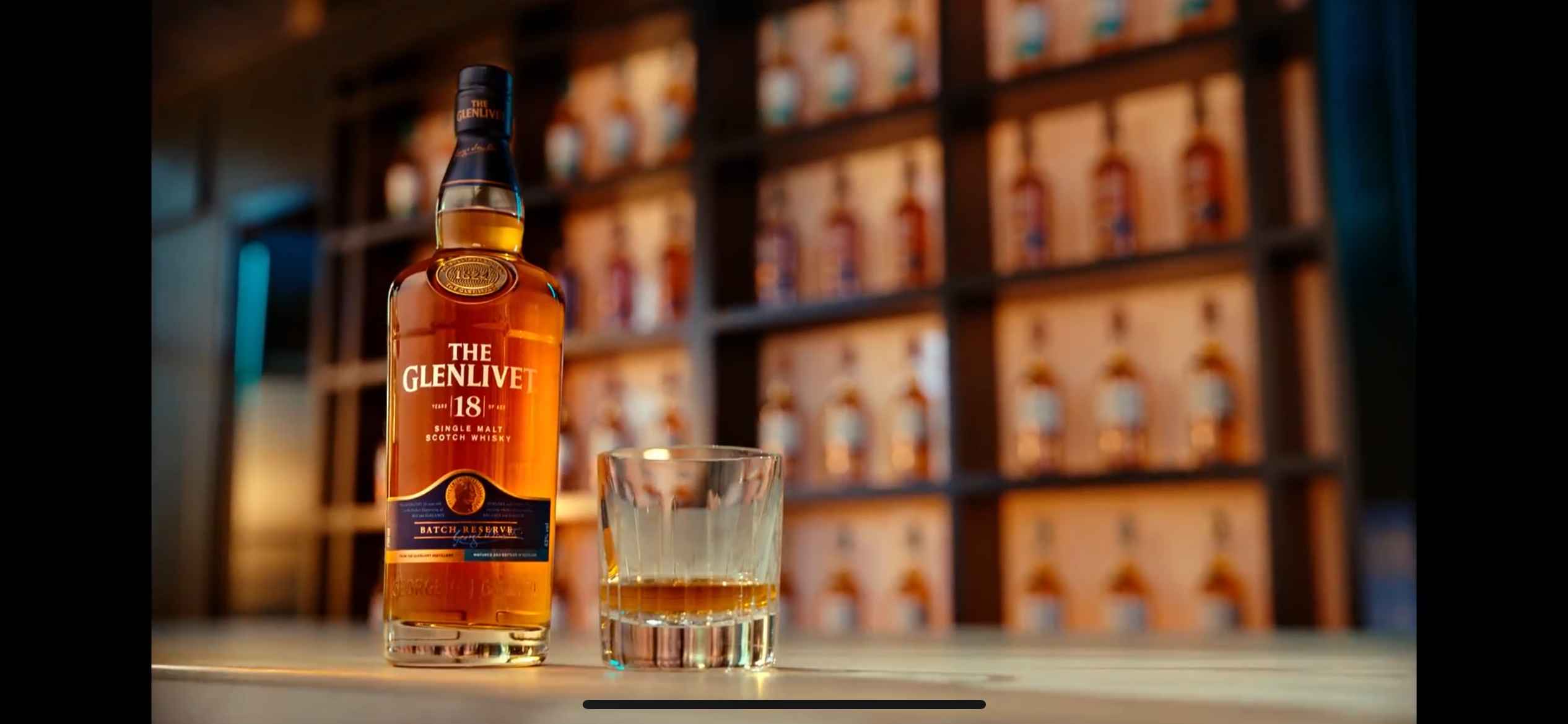 The Glenlivet 18 Year Old single malt Scotch whisky bottle and glass in front of a backlit bar display